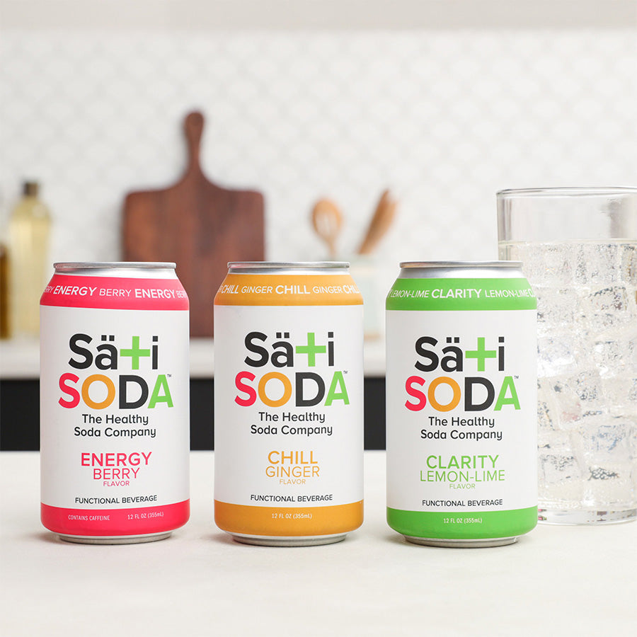 Three cans of Sati Soda on a kitchen counter with a glass of water.
